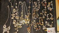 Full view of various necklaces and bracelets with multiple coin and charm pendants arranged on a black cloth