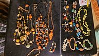 Overview of multiple necklaces and bracelets laid on black fabric showing various bead designs and colors.
