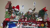 Wide view of the Christmas collection showing Department 56 building, trees, Jim Shore Santa and assorted figurines and stockings on table