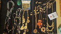 Lot of vintage necklaces with owl theme, multiple gold-tone necklaces, multi-strand bead necklaces, and matching earrings on black fabric.