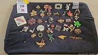 Top-down photo showing the entire assortment of more than 30 pins and brooches laid out on a dark fabric background