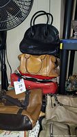 Stack of assorted pocketbooks in various colors and styles on a carpeted floor next to a fan and shelf.