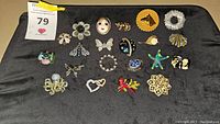 Overview of pins and brooches laid out on dark fabric including rhinestone butterfly, floral, face, starfish, octopus, animal pins
