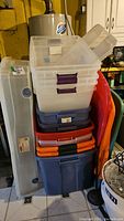 Totes stacked in basement corner including clear and blue Rubbermaid totes with various lids