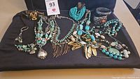 Overview of the turquoise jewelry lot with various necklaces and bracelets displayed on black cloth including silver and multicolored stones.