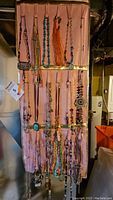 Full view of multiple necklaces on a fabric hanging organizer. Various colors including turquoise and orange beads and pendants.