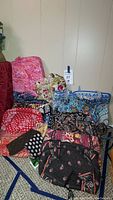 Full view of collection showing multiple Vera Bradley bags in different floral and colorful designs arranged together on carpet.