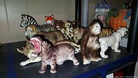 Shelf showing a variety of vintage ceramic wildlife animal figurines including hippopotamus, ape, tiger, fox, and zebra.