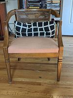 Front view of wooden accent chair showing cage-style cane back and peach seat cushion with decorative black and white pillow.