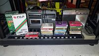 Two vintage carry radios side by side with cassette tapes and sealed VHS tapes arranged in front on a shelf.