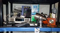 Shelf showing a collection of electronics and accessories including boxed Sony Dream Machine, calculators, a desk clock, and cleaning tools.