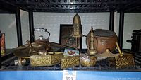 Photo showing several vintage brass and copper decorative items including vases, trivet, fish figurine, and kettle on shelving
