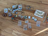 Wide shot showing assortment of costume jewelry including earrings, bracelets, cufflinks, pins, watches, and mini perfume bottles spread on floor.