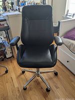 Front view of a black leather office chair with padded armrests and chrome base with wheels.