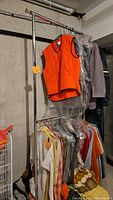 Full view of adjustable metal clothes rack holding various clothes in a basement area.