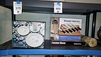 Shelf with boxed Sango Wild Flowers dish set and Greenwood Kitchen Forever Sharp gourmet knife set with bamboo paper towel roll