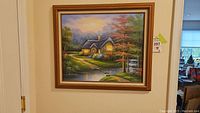 Framed oil painting showing a lit cottage with sharp details on trees, pond, and sky.