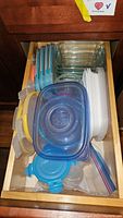 Top drawer filled with multiple plastic food storage containers with lids in varying sizes and colors, as well as several clear glass baking dishes.