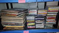 Stacked vinyl records and multiple stacks of CDs on blue shelves showing condition and quantity
