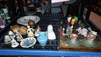 Wide view of all items in lot including Roseville candleholders, Royal Daulton balloon man figurine, small pitcher, bowl, and assorted small figurines arranged on a table.