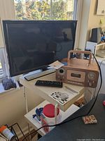 Samsung LED TV on small table with remote and manual, next to Studebaker CD radio cassette recorder with wooden finish and handle.