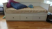 Front view of the wood twin trundle bed with cushions and 3 storage drawers visible, beige mattress, and pillows on top.