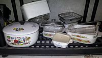 Full lot of vintage CorningWare and bakeware on shelving including lidded pot, glass baking dishes and rooster tin