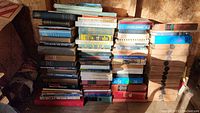 Stack of multiple vintage hardcover books piled in a shed, some dirty and dusty