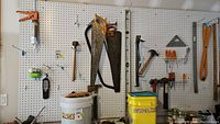 Photo of various hand tools hanging on pegboard including saws, hammers, levels, rulers, and other tools