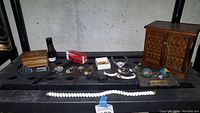 Photo showing an array of vintage wristwatches, wooden music boxes, necklaces, jewelry loupes, and assorted decorative items on a black surface.