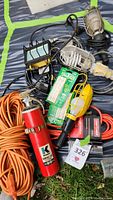 Photo showing assorted work lights with protective cages, orange extension cords, red fire extinguisher, and a boxed halogen light bulb.
