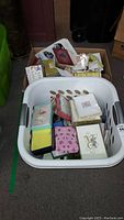Top-down view of white plastic laundry basket filled with various boxed and loose greeting cards and stationery.