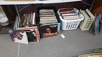 Photo showing a wide range of vinyl records collection stacked on the floor beneath a table, with visible album covers including The Isley Brothers and Al Green.