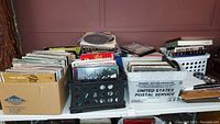 Photo showing large collection of vinyl records in boxes and crates on table, some album covers visible.