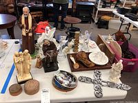 Photo showing a variety of religious figurines, crosses, small boxes, and decorative trays gathered on a white table.