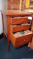 Wooden 3 drawer storage cabinet with all drawers pulled open showing sewing notions inside each drawer