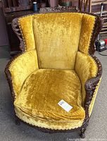 Full front view of vintage armchair showing plush mustard yellow velvet fabric and carved wood frame with wear