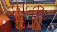 Two vintage wooden sleds with metal runners and wood slat seats shown indoors near a window.