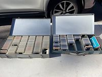 Top-down view of two open metal slide holder boxes showing contents: one box with rows of white slide mounts; the other box with assorted photographic slides and smaller organizers.