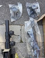 Photo of partially assembled black metal speaker tripod with visible tightening knobs and mounting hardware pieces wrapped in plastic.