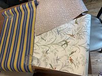Three rolls of wallpaper showing different patterns: blue/yellow stripes, bird motif, and taupe swirl