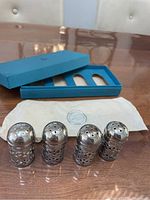 Four silver plated salt/pepper shakers in front of blue box and folded tissue paper with Birks logo