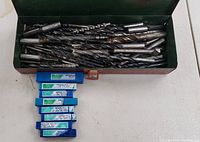 Open green metal box showing various concrete drill bits and blue labeled plastic cases of bits beneath