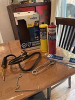 Full kit overview showing torch with hose, two fuel cylinders, torch stand, spark lighter, and rods on table with packaging box.