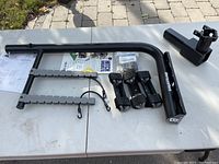 Full view of all components of the Barrecrafters hitch mount rack laid out on a table including hitch bar, rack arms with notches, locking clamps, hardware bag, and instructions.