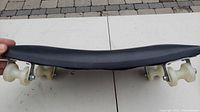 Top side view of car creeper showing contoured black cushion surface and four white wheels for mobility.