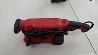Side view of the red Eastvolt belt sander showing its compact body, handle, and attached power cord.