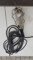 Top view of the hanging construction light with coiled long black cord beneath it, metal protective cage visible.