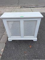 Front view of white wooden heater cover showing two decorative perforated panels and flat top.