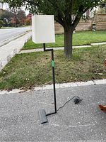 Modern black metal standing lamp with cream rectangular fabric shade, photographed outdoors from two angles.
